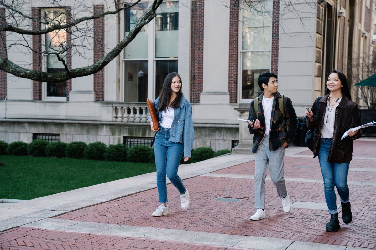 Three students happily walk through their university campus, holding textbooks.