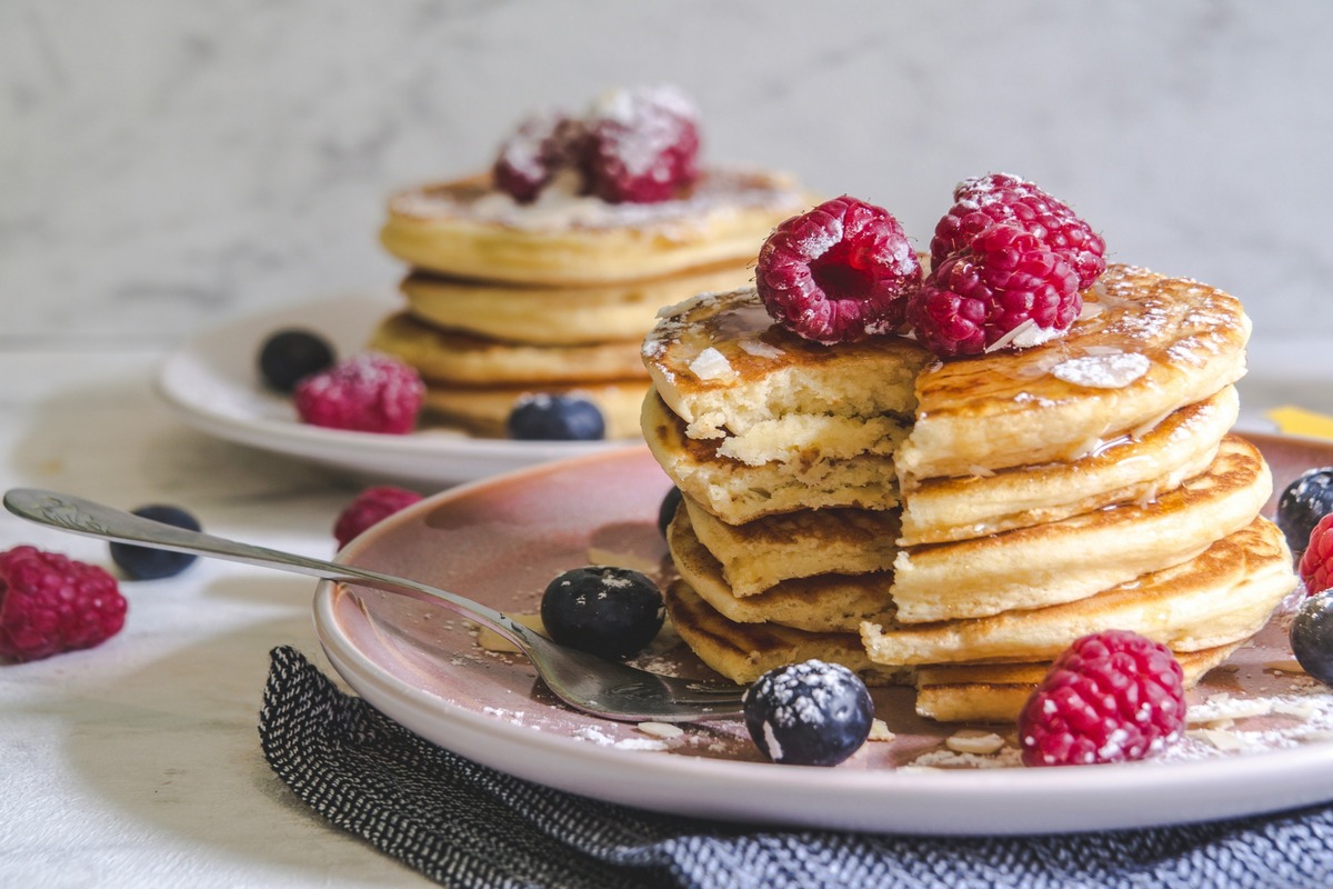 Two stacks of fluffy pancakes rest on pretty plates, covered in fresh fruit.