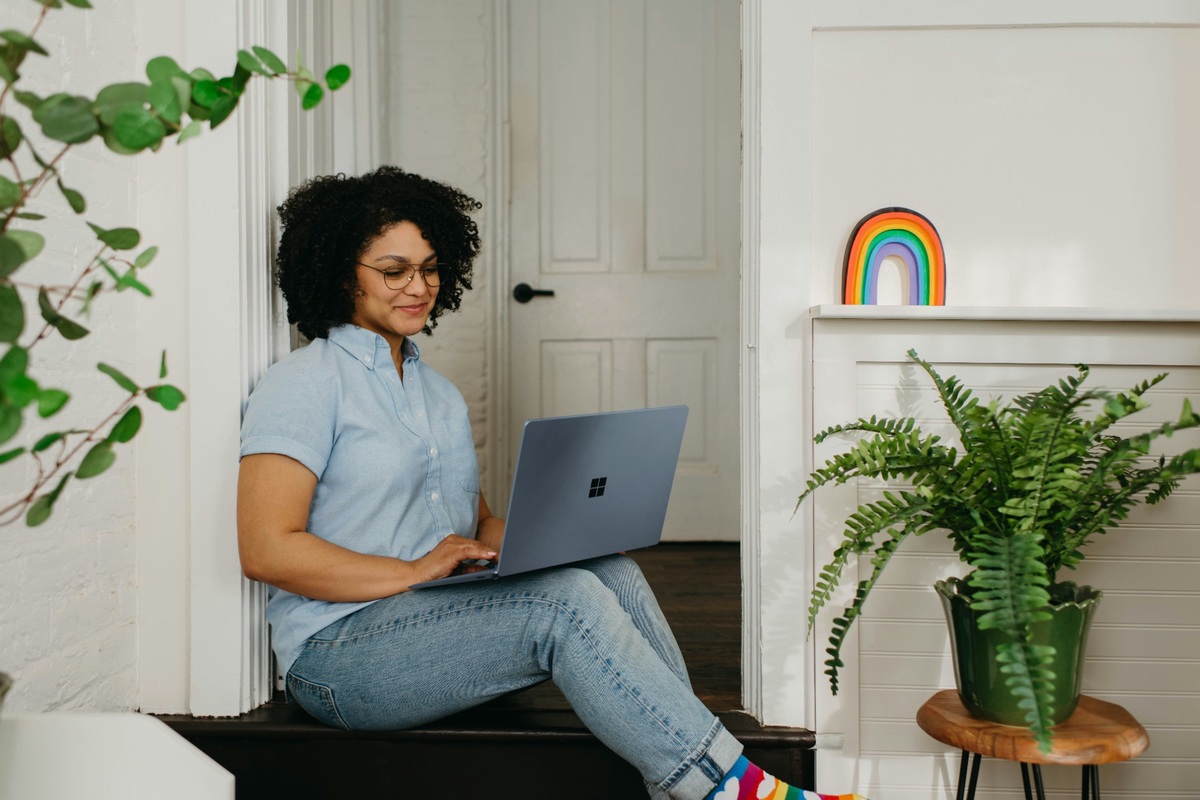 A Black woman smiles as she researches student finance on her laptop at home.